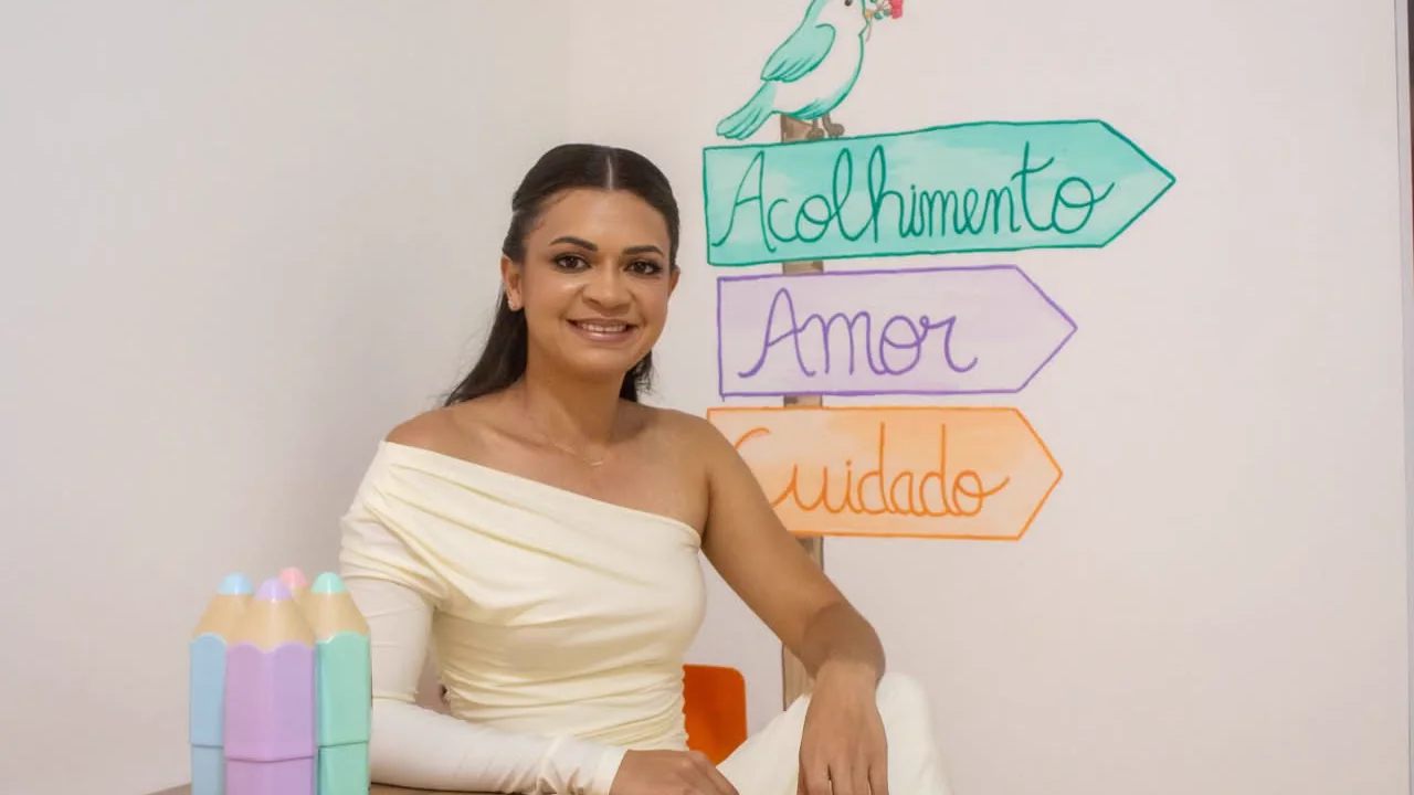 Glaucia Amanda sentada à mesa, diante de uma parede pintada com placas escritas acolhimento, amor e cuidado